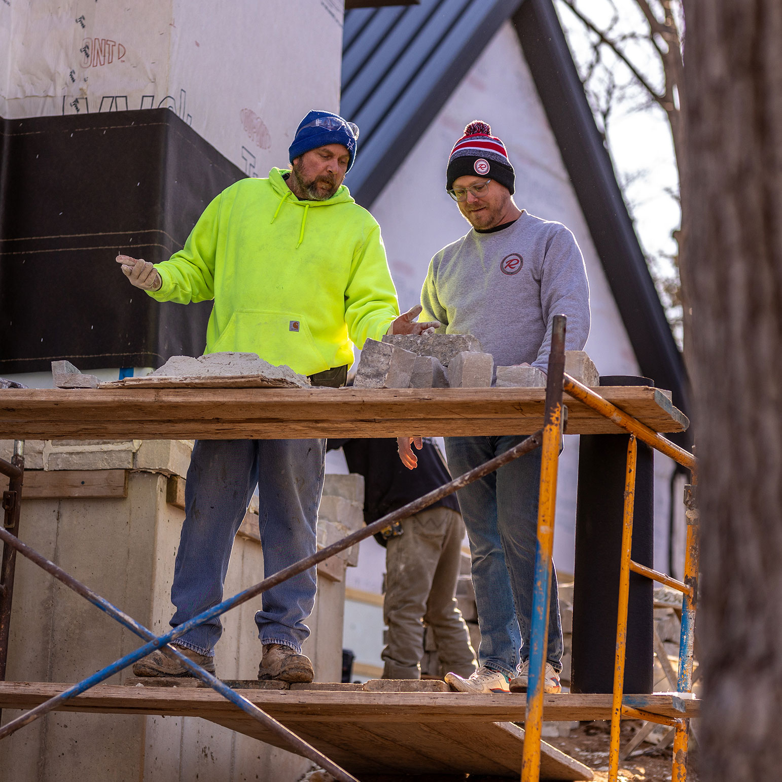 Brock Rademann and a stone mason talking together in front of a home where stone veneer is being installed